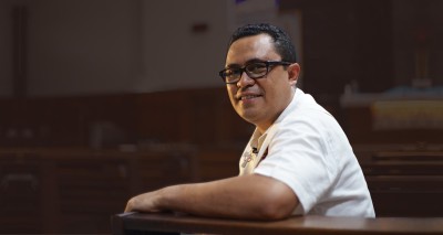 man smiling, sitting in a pew, with altar and pulpit in background