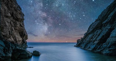 Ocean water between two steep mountains under a dark, starry sky showing the Milky Way