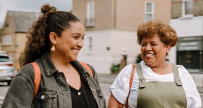 Two women walk down the street chatting and smiling.