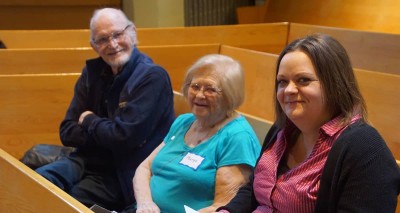 Three people of different ages sitting in a pew.