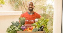 Man wearing a T-shirt that says "Delivery" holding a box of fresh fruits and vegetables.