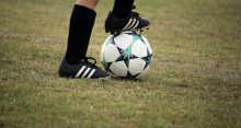 Young player standing on soccer field with foot on ball.